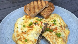 En tallerken med omelet og ristet brød, en vase med røde blomster, og en menustativ i baggrunden.