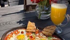 En tallerken med brød, æg og tomater, ledsaget af et glas appelsinjuice.