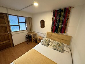 A bedroom with a bed, a desk, a chair, a window, and a curtain. - Siete Cuartones 290 (Cusco)
