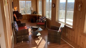 Une pièce chaleureuse aux murs en bois et aux grandes fenêtres, meublée de chaises en osier et d’une petite table.