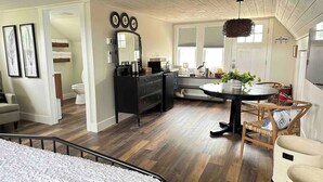 A modern bedroom with a large bed, a dresser, a vanity with a mirror, and a dining area with a table and chairs.