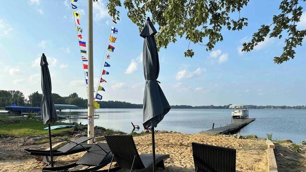 Une plage avec des chaises longues et des parasols, une jetée et des drapeaux.