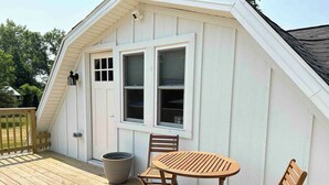 Un espace extérieur abrité, doté d’une terrasse en bois, d’une table avec des chaises et d’un grand bac à fleurs.