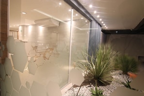 Interior moderno com divisórias de vidro, design geométrico na parede e plantas em vasos.