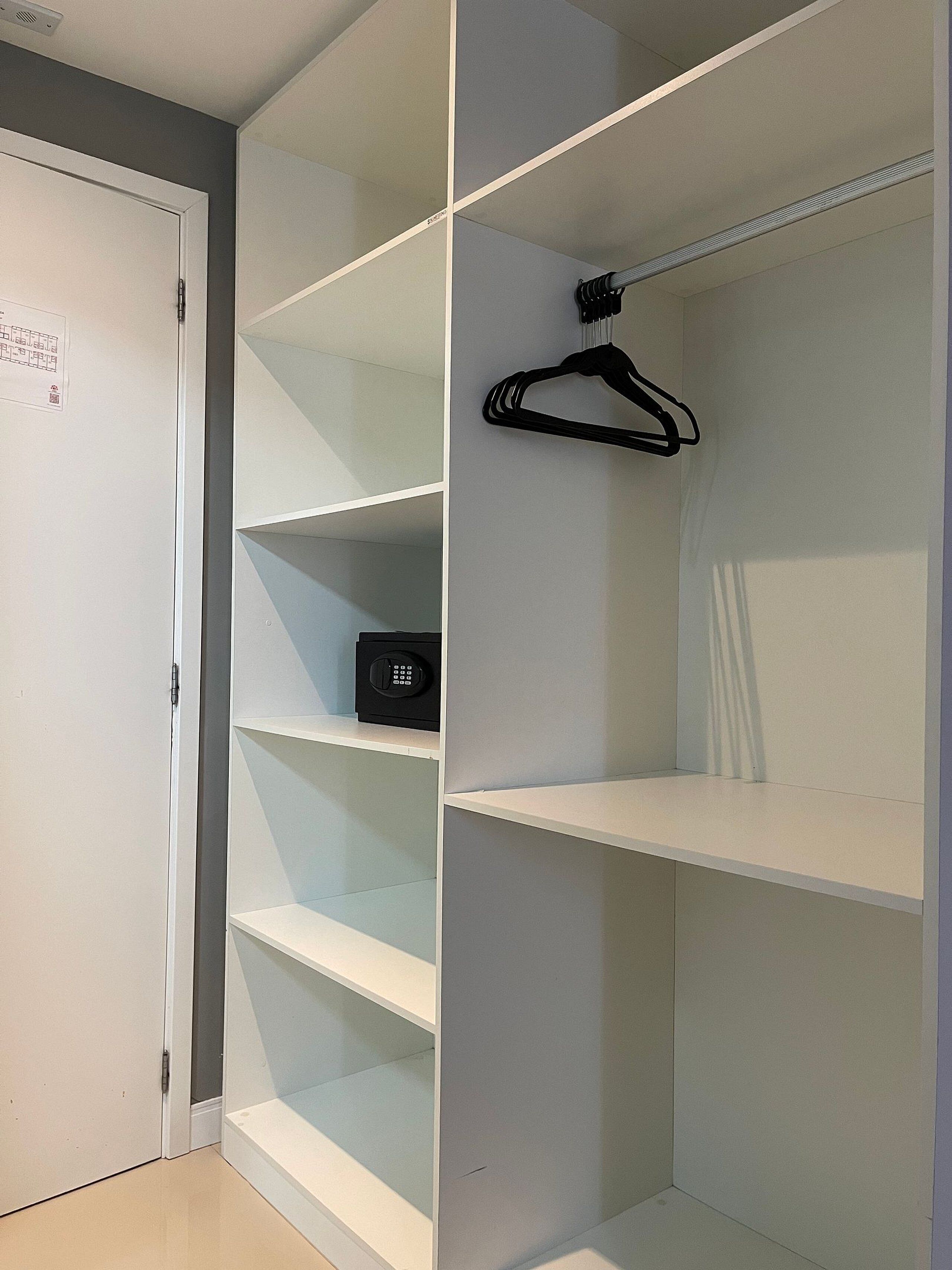 Ein begehbarer Kleiderschrank mit weißen Regalen, einem schwarzen Kleiderbügel und einem Safe.