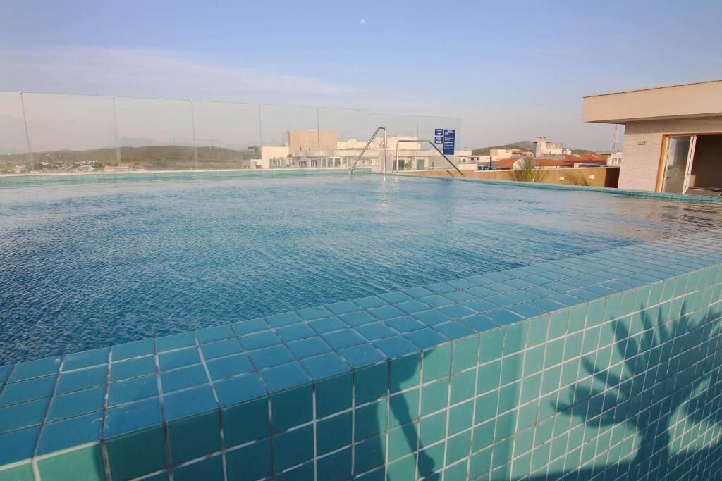 Une piscine dont les bords sont recouverts de carreaux, avec un plongeoir, et qui offre une vue sur les bâtiments en arrière-plan.
