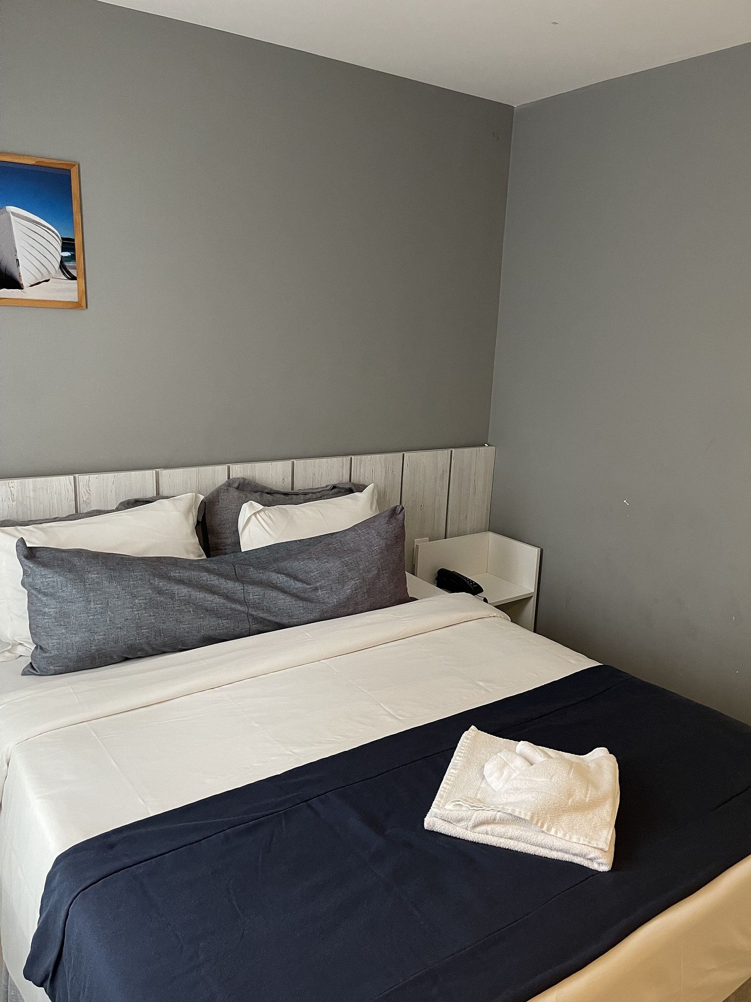 Una camera d'hotel con un letto, cuscini, un comodino e un quadro appeso al muro.