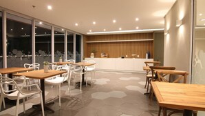 A modern dining area with hexagonal floor tiles, wooden tables, white chairs, and a reception desk. - hihome - Royale (Cabo Frio)