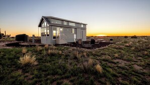 Une maison moderne dotée d’une grande terrasse, d’un espace extérieur couvert et offrant une vue sur le coucher de soleil.
