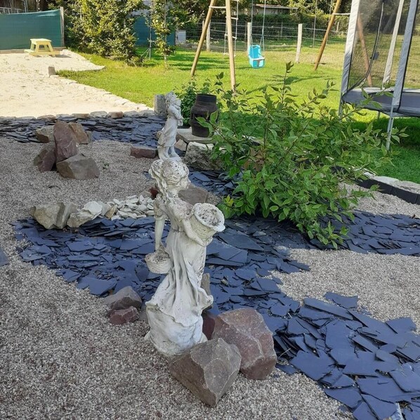 Un jardín con una estatua, rocas y un columpio.