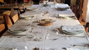 Een eettafel gedekt met wijnglazen, borden en bestek, met een open haard op de achtergrond.