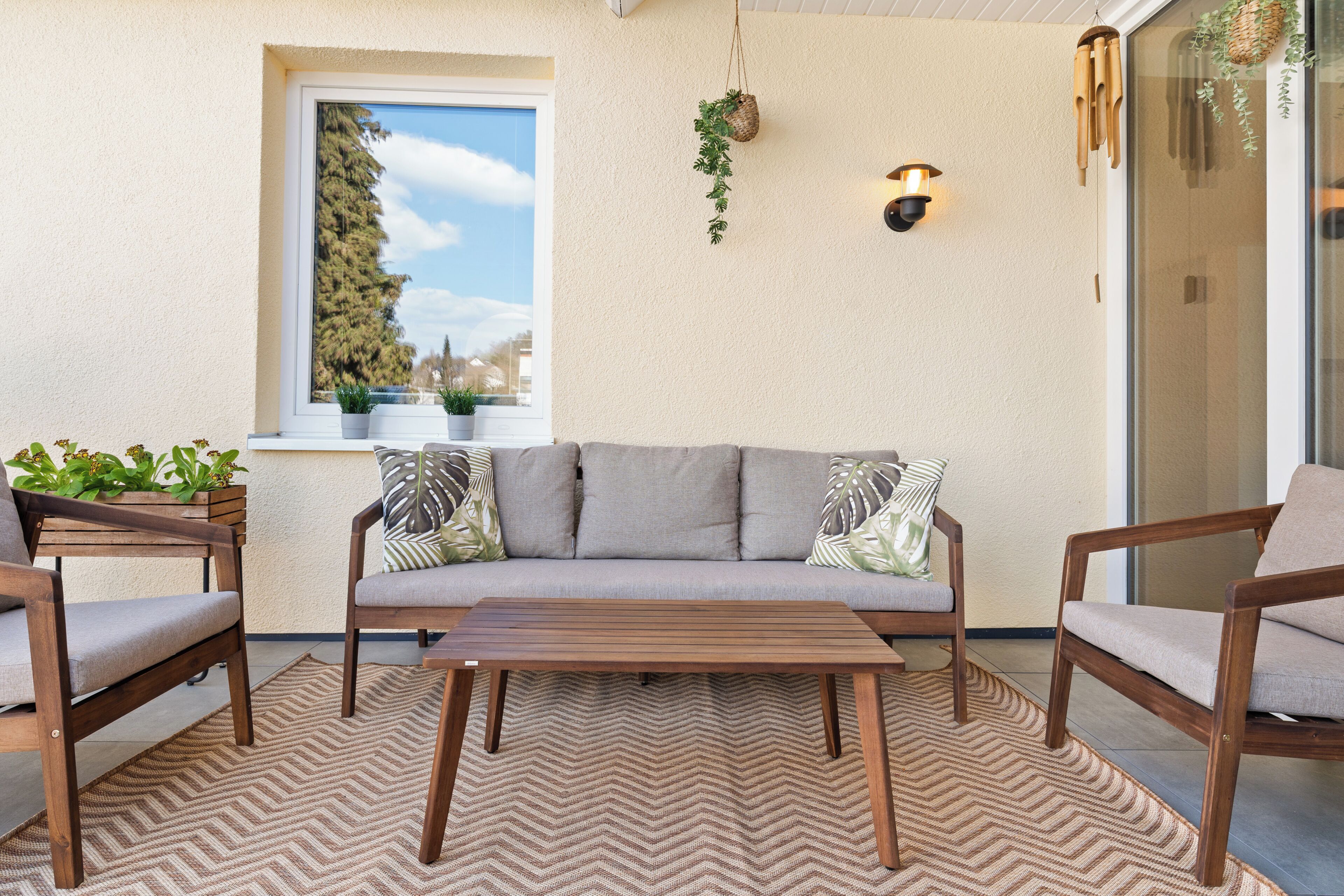 Un patio acogedor con un sofá, dos sillones, una mesa de madera y un tapete estampado.