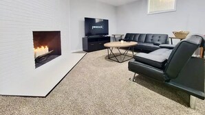 A modern living room with a fireplace, a flat-screen TV, a black leather sofa, and a coffee table. - 5BD Cozy, SouthGlenn Gem, Yard, Games, Shops, close to Downtown Littleton&Denver (Centennial)