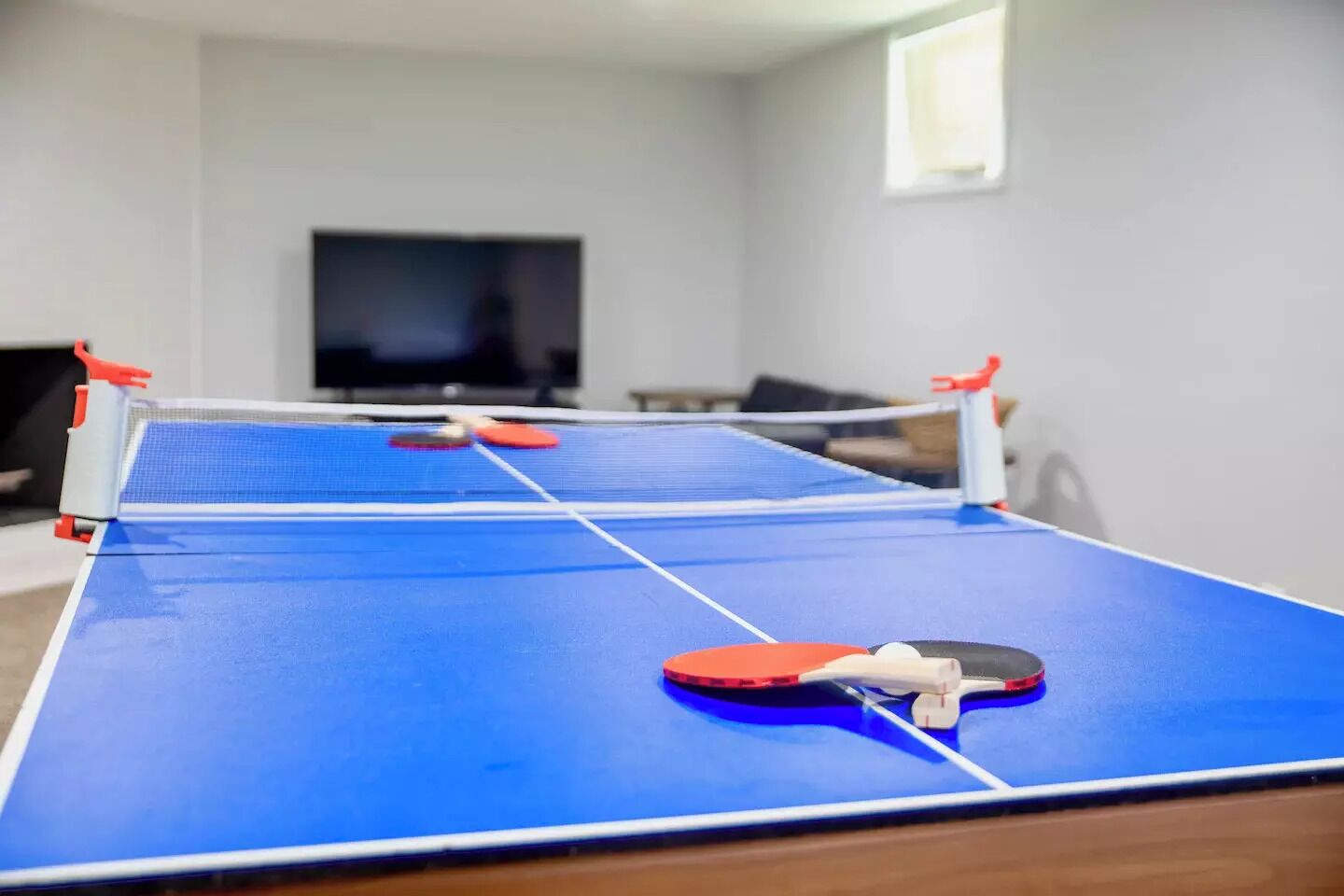 A ping pong table in a room with a television in the background.