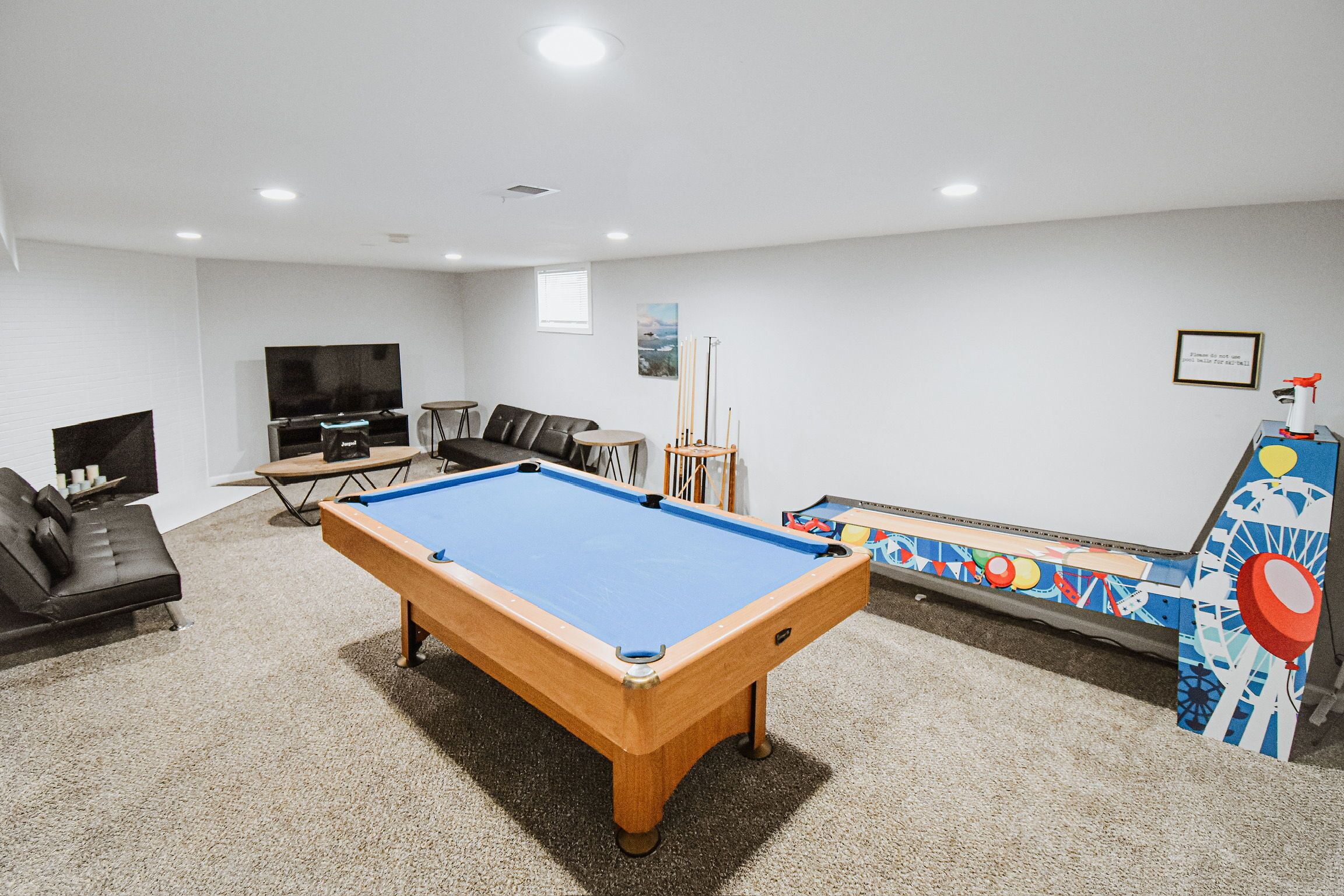 A pool table in a room with a sofa, a television, and a pinball machine.