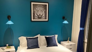 Ein Schlafzimmer mit einem großen Bett, zwei Nachttischen, einem gerahmten Bild an der Wand und einem blauen Vorhang.