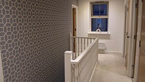 A hallway with a patterned wall, a white railing, and a window with a view.