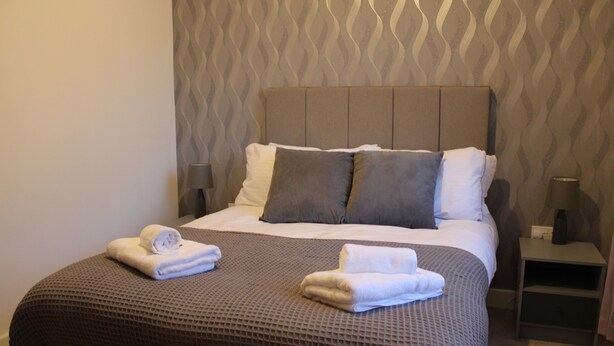 A neatly made bed with a brown textured bedspread, two pillows, and two folded towels on the foot of the bed.