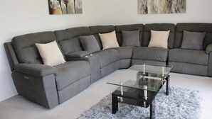 A modern living room with a grey sectional sofa, a glass coffee table, and abstract wall art.