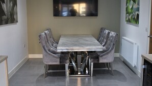A dining area with a table and four cushioned chairs, a large painting on the wall, and a radiator.