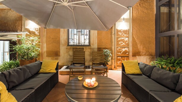 A cozy outdoor seating area with a round table, two sofas, and a large umbrella providing shade. - Villa Michelangelo, your home in the heart of the eternal city (Roma)