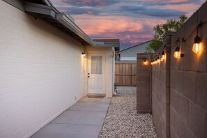 A narrow pathway leading to a white door, surrounded by a wooden fence and a white wall.