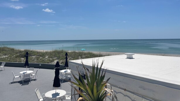 Une terrasse sur le toit avec des sièges extérieurs, une vue sur la plage et un ciel dégagé.