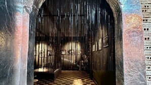 An arched doorway with a checkered floor, leading to a room with a barred window and a bench.