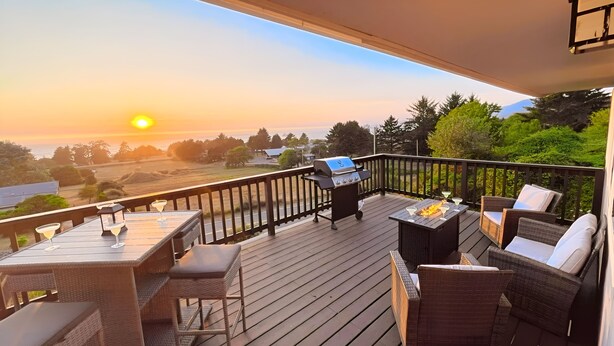 Eine Terrasse mit Grill, Gartenmöbeln und Blick auf den Sonnenuntergang.