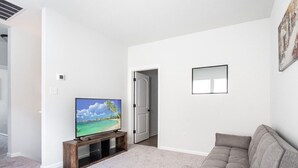 Un salon avec un téléviseur à écran plat posé sur un meuble en bois, un canapé gris et une porte donnant sur une autre pièce.