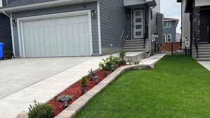 A modern two-story house with a large garage, a well-maintained lawn, and a stone border along the driveway. - 2 Bedroom 1.5 Bathroom Brand New, Tranquil Suite: Your Gateway to Rockies & City (Calgary)