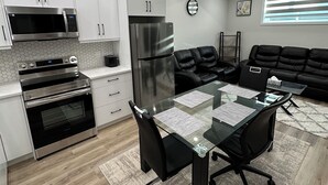A modern kitchen with white cabinets, stainless steel appliances, and a dining area with a glass table and black chairs. - 2 Bedroom 1.5 Bathroom Brand New, Tranquil Suite: Your Gateway to Rockies & City (Calgary)