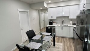 A modern kitchen with white cabinets, a stainless steel refrigerator, and a dining area with a glass table and black chairs. - 2 Bedroom 1.5 Bathroom Brand New, Tranquil Suite: Your Gateway to Rockies & City (Calgary)