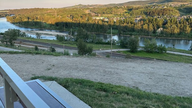 A bench overlooking a river with a bridge and a town in the distance. - 2 Bedroom 1.5 Bathroom Brand New, Tranquil Suite: Your Gateway to Rockies & City (Calgary)