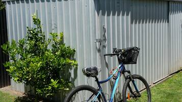 A blue bicycle with a basket and fenders parked against a corrugated metal shed.