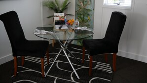 A glass-top table with two black chairs, a decorative plant, a vase with flowers, and a small bowl of oranges. - The Pool House Bed & Breakfast - 50 sq Kitchenette Studio - Near Marine Parade (Napier)