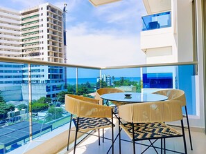 A balcony with a glass railing, round table, and four chairs, overlooking a cityscape and the sea. - Exclusive Apartment in Beach Club (Gaira)