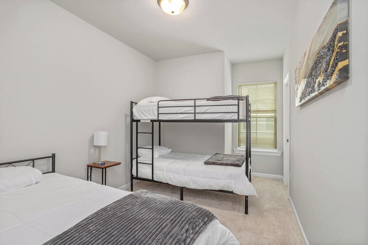 Une chambre avec des lits superposés, une table de chevet avec une lampe et une fenêtre avec des stores.