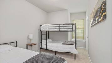 Une chambre avec des lits superposés, une table de chevet avec une lampe et une fenêtre avec des stores.