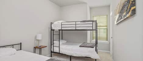A bedroom with bunk beds, a bedside table with a lamp, and a window with blinds.