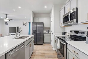 Une cuisine moderne dotée d’appareils électroménagers en acier inoxydable, d’un îlot central et de meubles blancs.