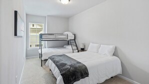 Quarto com duas camas beliche, janela com persianas, mesa de cabeceira com abajur e luminária no teto.