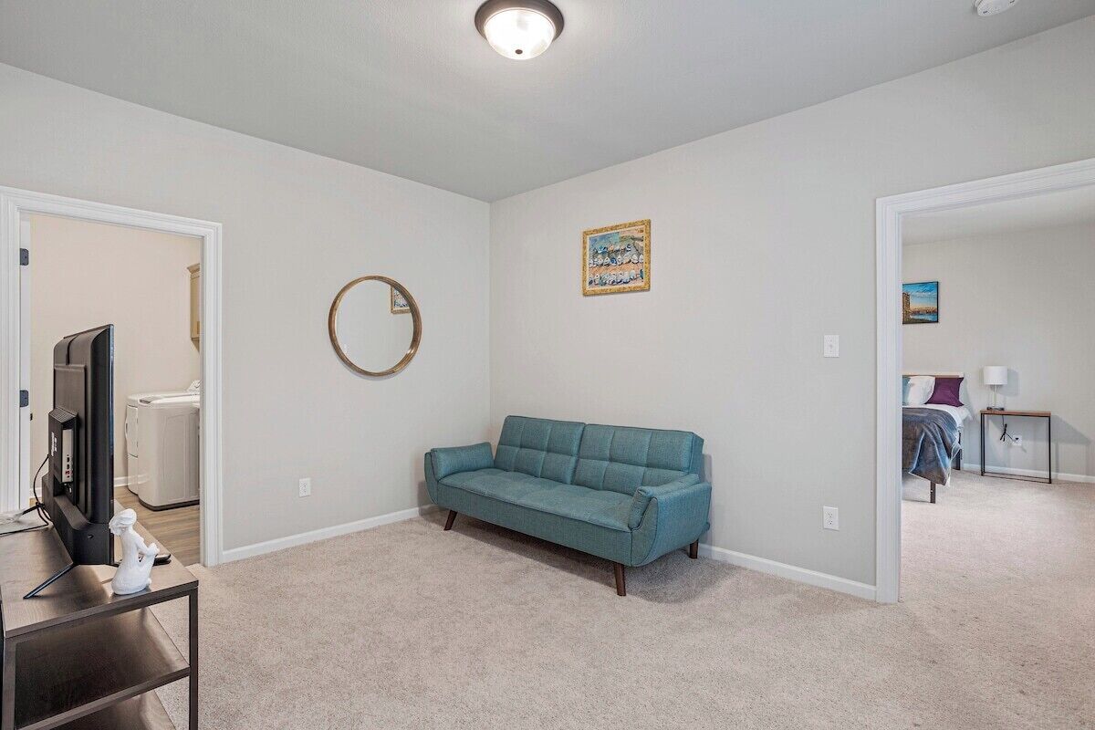 Une pièce avec un canapé de couleur turquoise, un téléviseur posé sur un meuble, un miroir rond et un tableau accroché au mur.
