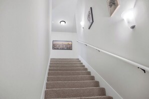 Un escalier recouvert de moquette, doté d’une rampe, avec un tableau accroché au mur et un luminaire au plafond.