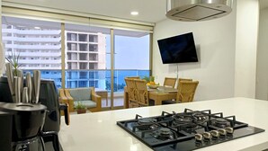 A modern kitchen with a gas stove, dining table, chairs, and a large window offering a view of a building and the sea. - Amazing Apartment in Beach Club - Samaria! (Gaira)