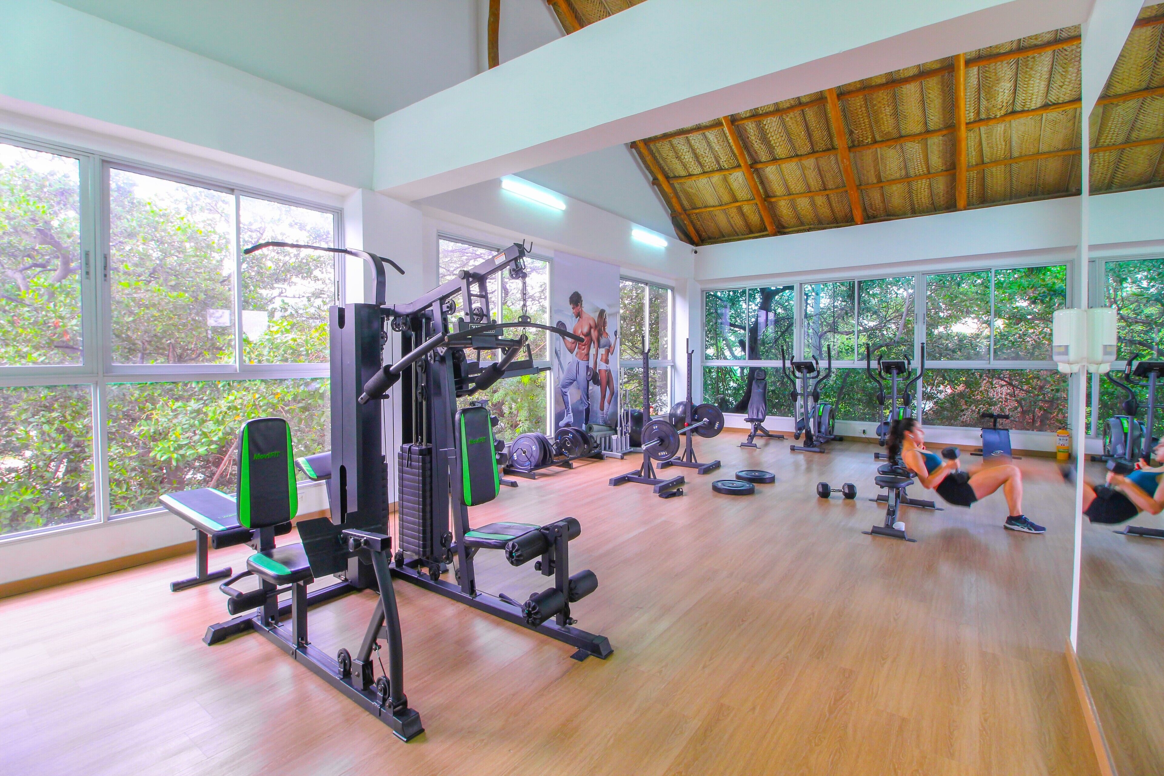 A gym with various exercise equipment, large windows, and a thatched roof ceiling.