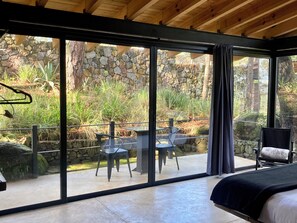 Quarto moderno com uma grande porta de vidro deslizante que dá para um pátio ao ar livre com uma parede de pedra, uma mesa e cadeiras.