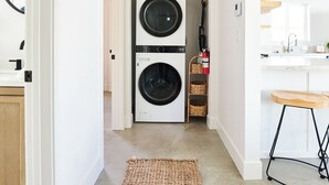A laundry room with two stacked washers and dryers, a fire extinguisher, and a kitchen area with a bar stool. - Private Guest House with Full Kitchen, 30 minutes to L.A. & Beach (Thousand Oaks)
