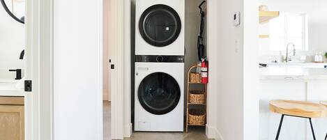 Une buanderie équipée de deux machines à laver et deux sèche-linge superposés, d’un extincteur et d’un coin cuisine avec un tabouret de bar.