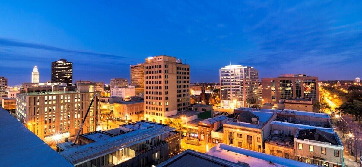 A cityscape at dusk with illuminated buildings and a clear sky.